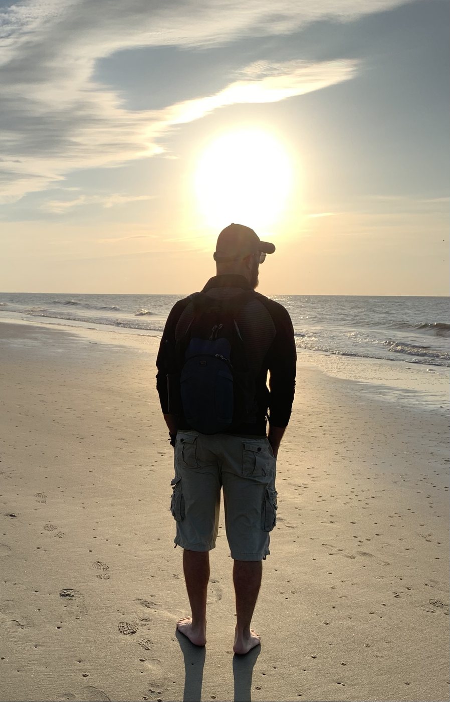 Russ barefoot on the beach facing the sunset
